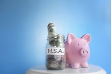 pink piggy bank and jar labeled HSA full of coins and bills