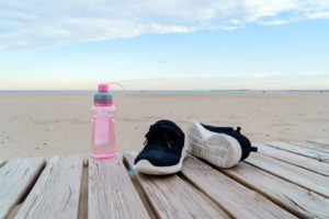 running shoes and water bottle near a beach