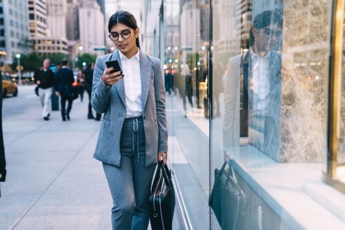 business woman walking in city while looking at device