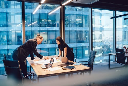 male and female business people looking over files at a desk in a high rise office