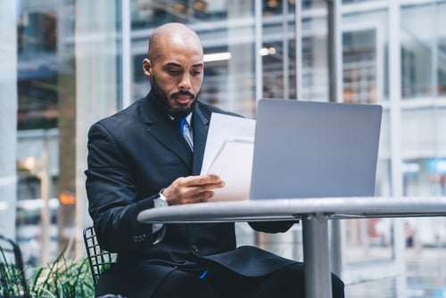 man in commerical building reviewing papers and laptop screen