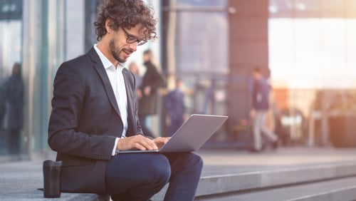 business man on city street sitting down with laptop open