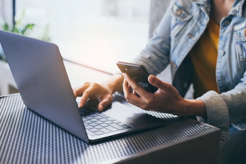 person looking at phone and typing on laptop