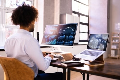 man at desk working on a computer with graphs on the screen