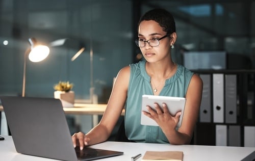 black woman accountant on laptop and tablet reviewing financial documents