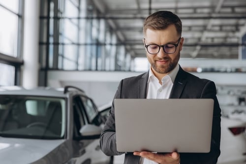 man holding open laptop walking through an auto dealership