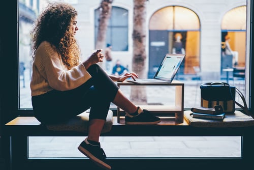 woman sitting by a window with a laptop open